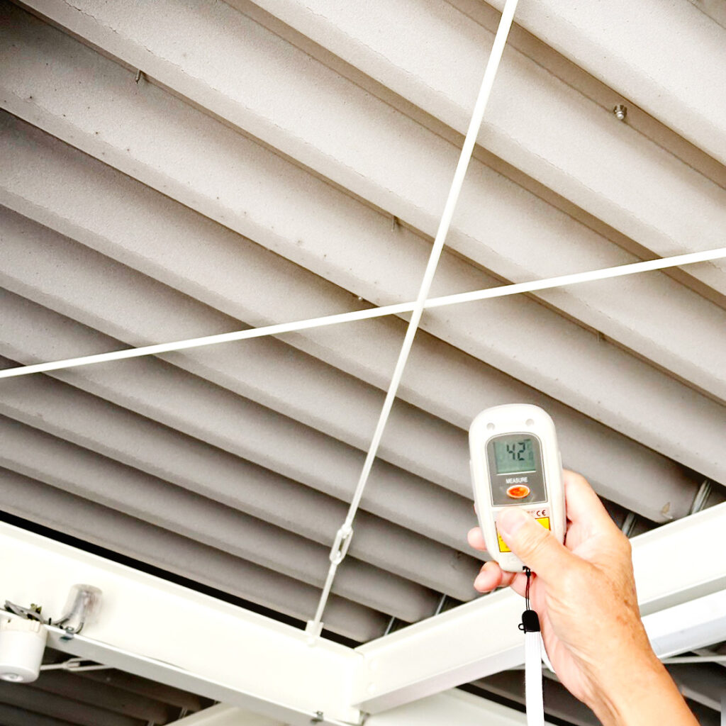 屋内から屋根の表面温度を計測している様子。計測器には42℃と表示されており、遮熱・断熱効果を確認している現場写真